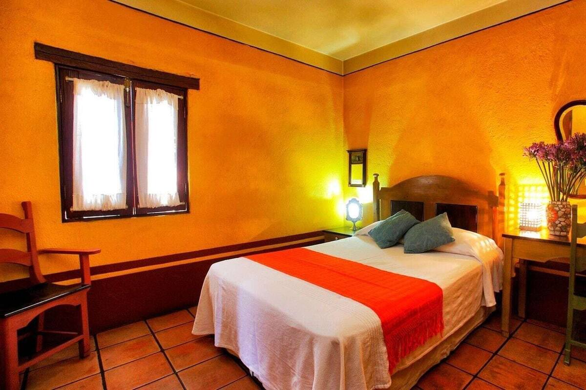 A hotel room with a bed, a chair, a desk, a mirror, and a window with curtains.