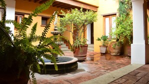 A courtyard with a fountain, potted plants, and a building with yellow walls and wooden beams. - Hotel Azucena (Oaxaca)
