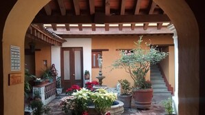 An outdoor courtyard with a wooden pergola, potted plants, a fountain, and a staircase. - Hotel Azucena (Oaxaca)