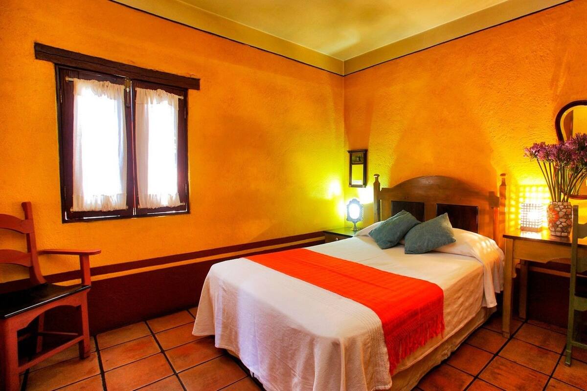 A hotel room with a bed, a chair, a desk, and a window with curtains.