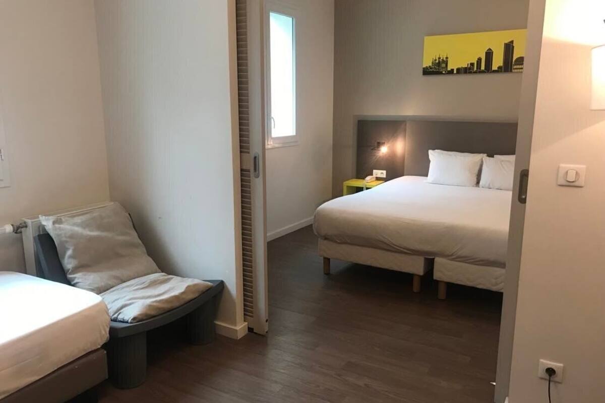 A bedroom with a bed, a chair, a bedside table, and a window.