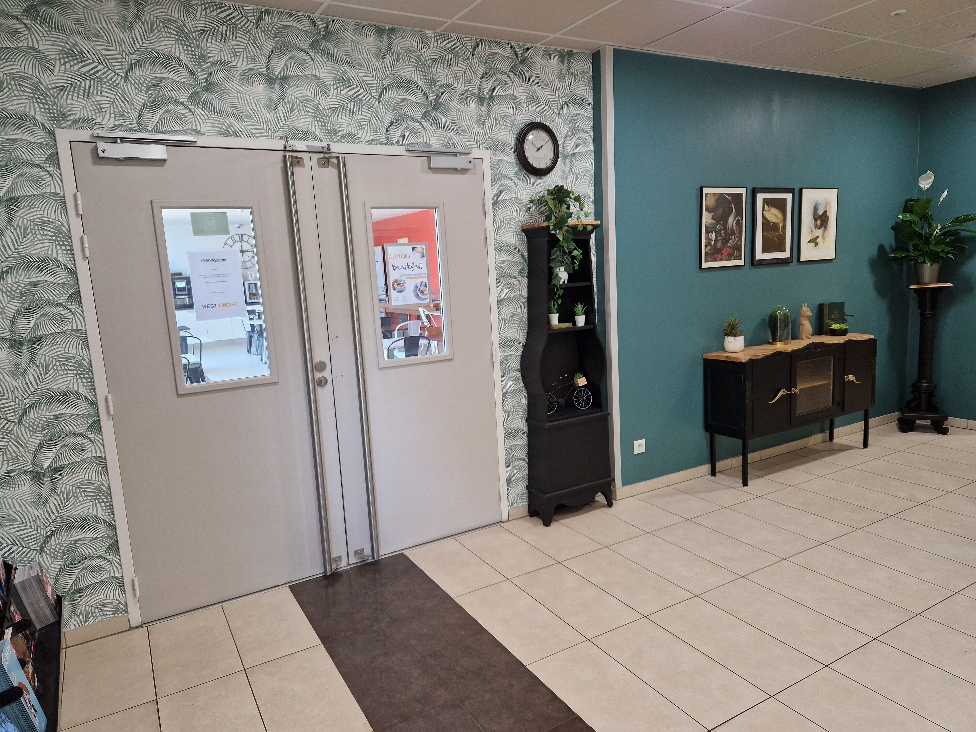 Un hall d’entrée avec un mur décoré de motifs, une horloge, un coin café et une plante.