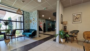 Een ruime lobby met een blauwe bank, rieten stoelen en potplanten.