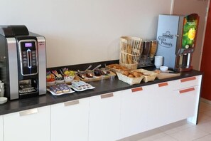 Una barra de desayuno con una máquina de café, exprimidor de frutas y diversas opciones de comida como pasteles y mermeladas.