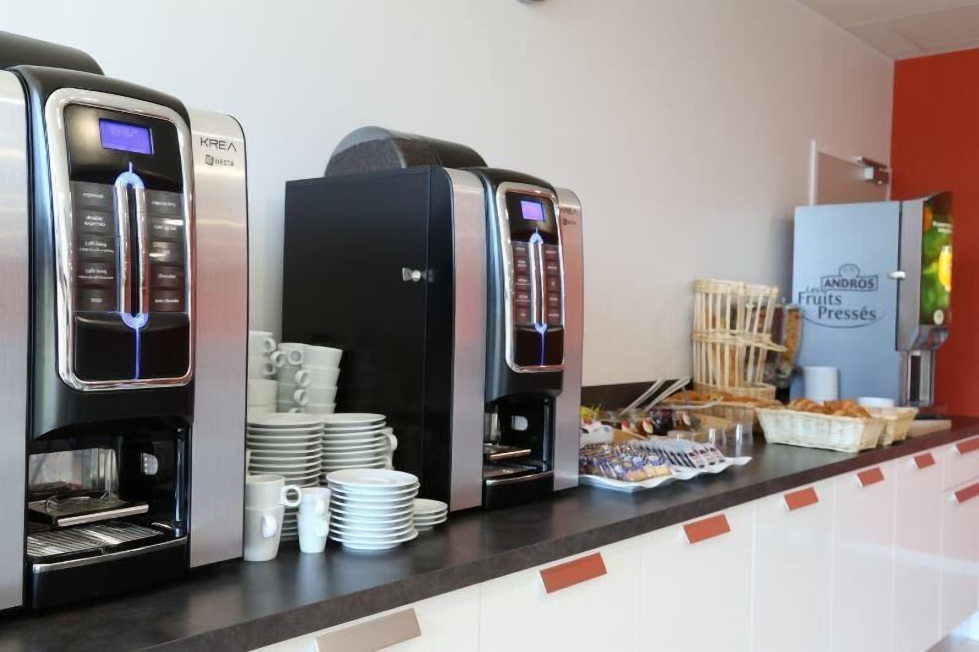 Een koffiehoek met meerdere koffiemachines en een koelkast met de tekst 'Andros Fruits Presses'.