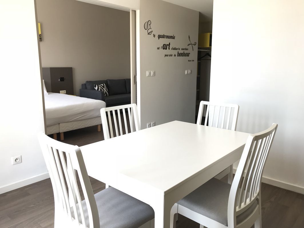 A dining area with a white table and chairs, a grey sofa in the background, and a wall with a decorative sign.