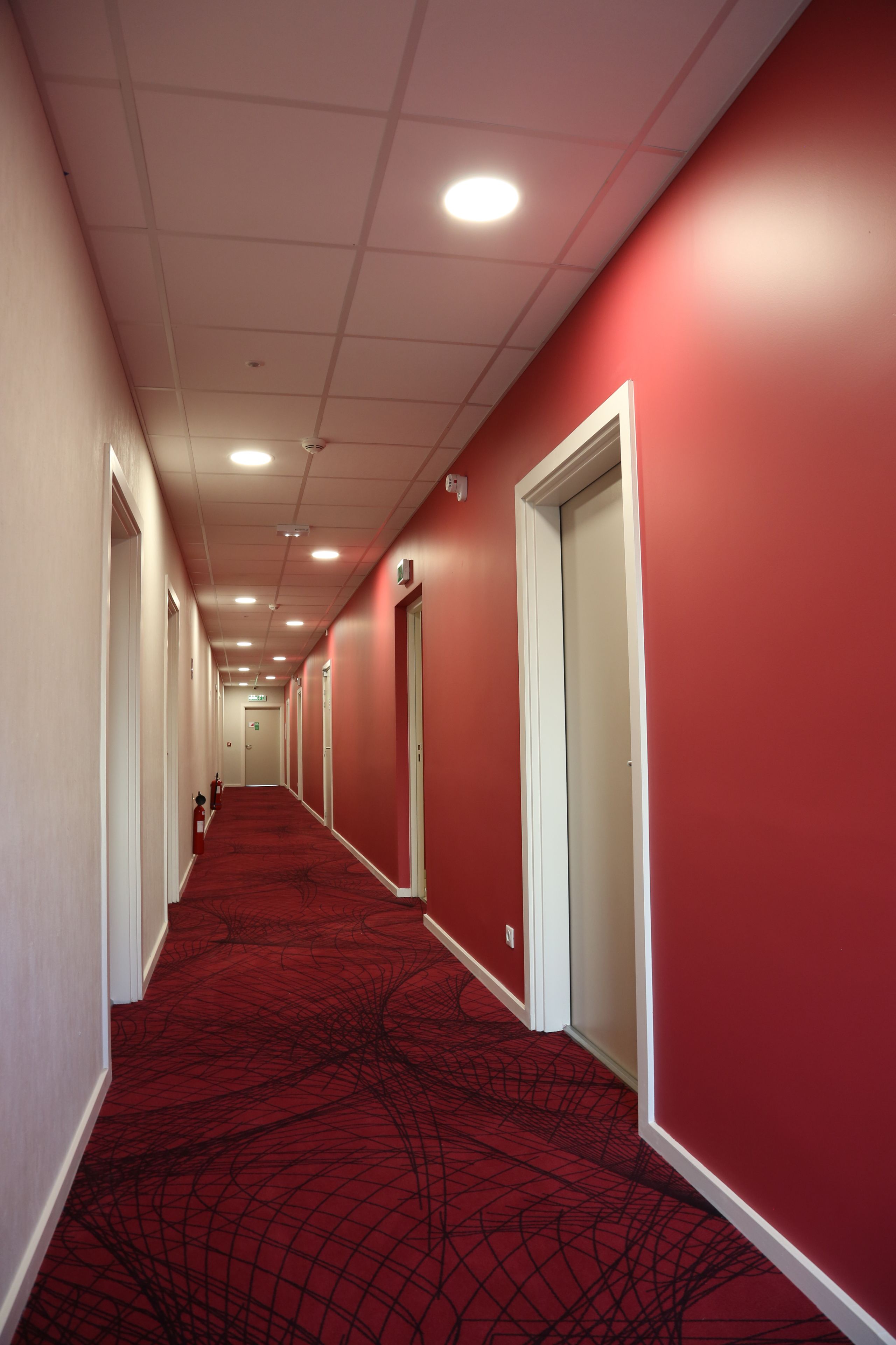 Un pasillo con paredes rojas y una alfombra estampada, que conduce a puertas al final.
