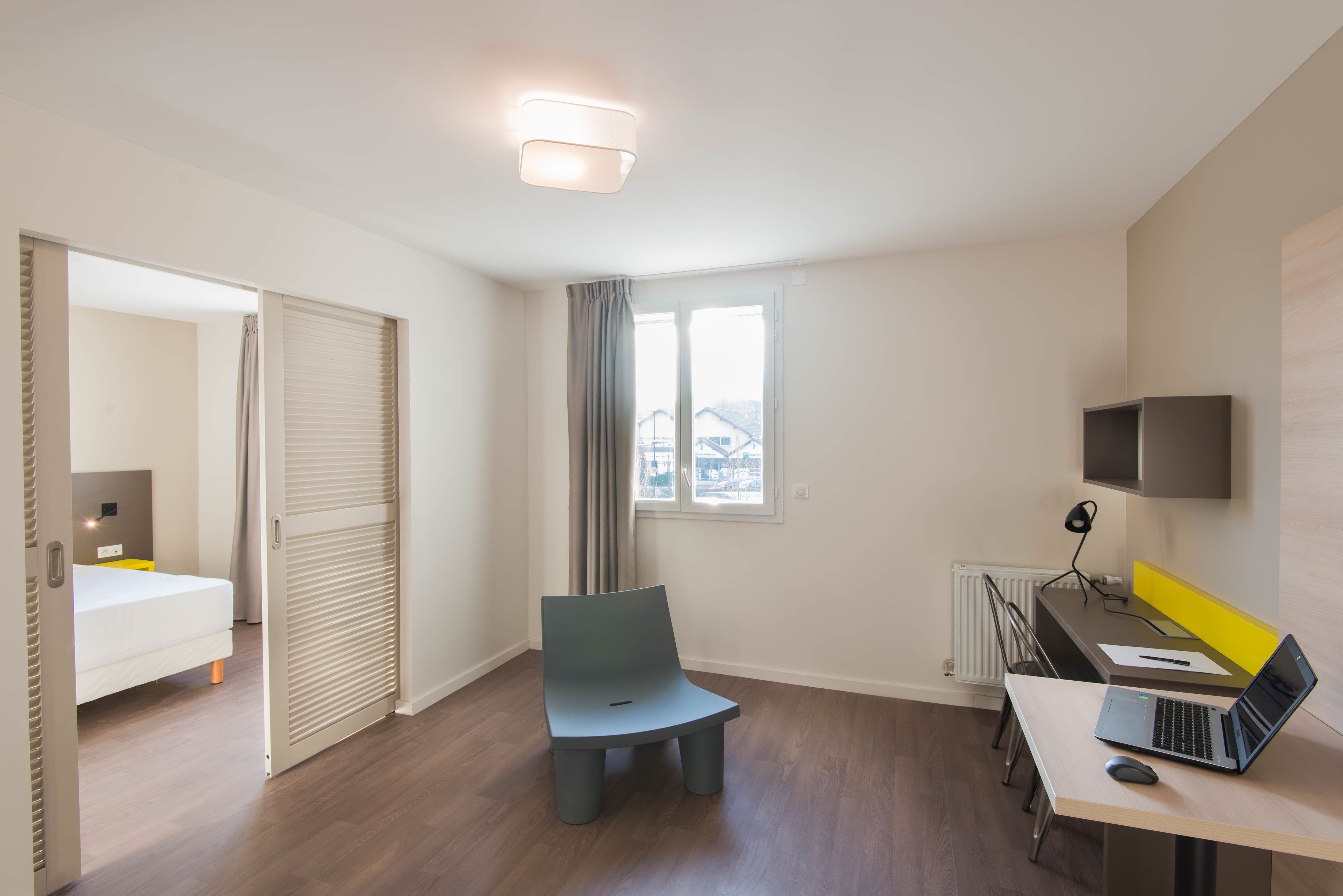 A modern hotel room with a bed, a desk with a laptop, a chair, and a TV.
