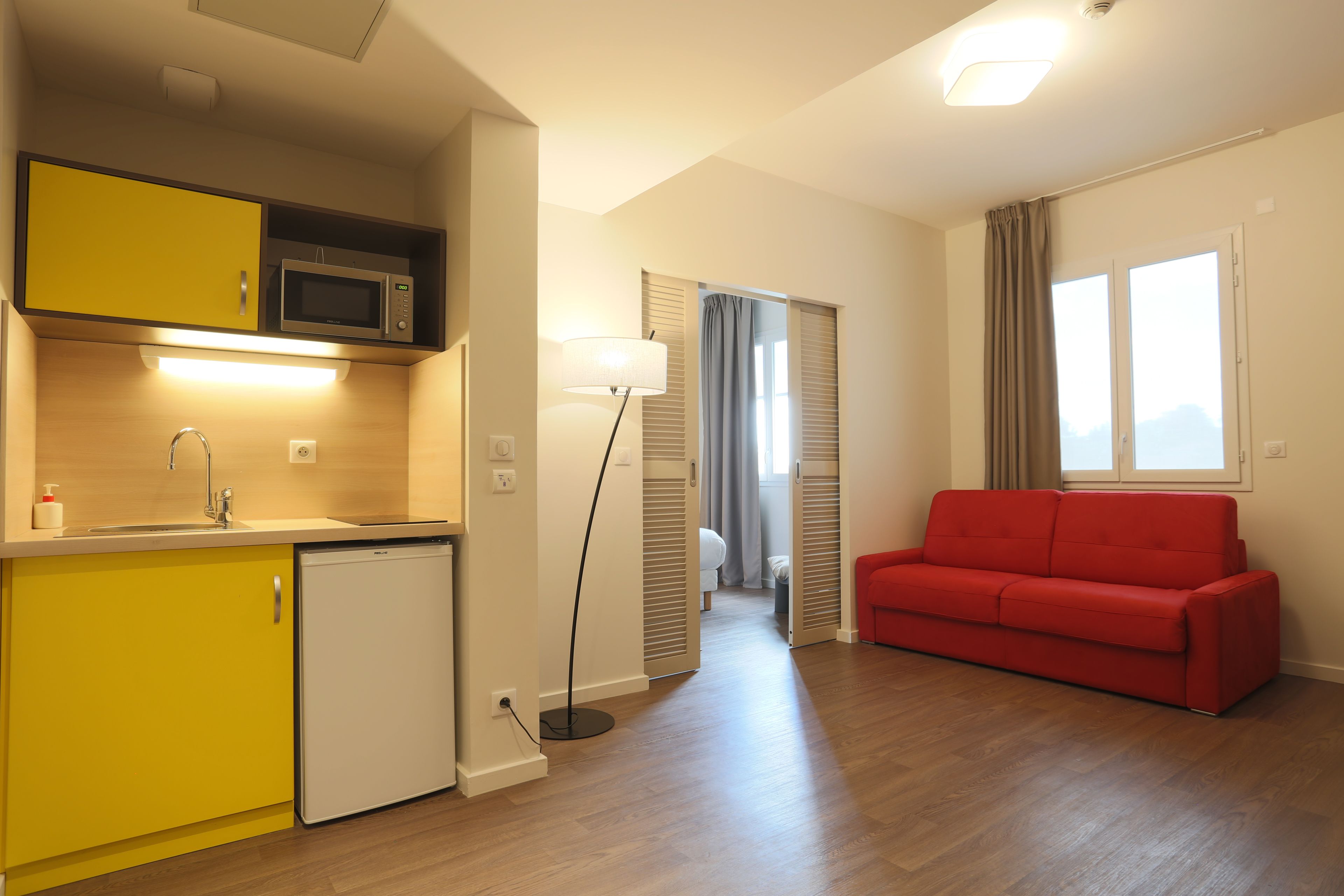 A compact living space with a kitchenette, a red sofa, and a floor lamp.