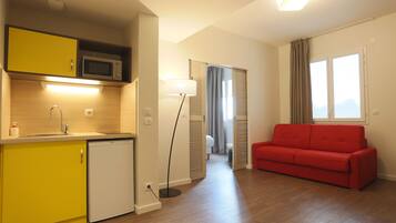 A compact living space with a kitchenette, a red sofa, and a floor lamp.