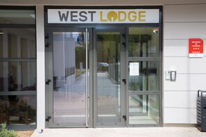 La entrada al hotel West Lodge, con una puerta de cristal y un cartel arriba.