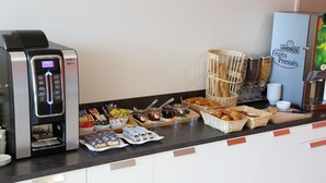 Een ontbijtbuffet met een koffieapparaat, brood, gebak en toevoegingen.