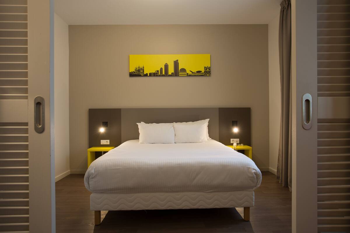 A hotel room with a large bed, a cityscape painting on the wall, and two bedside tables with lamps.