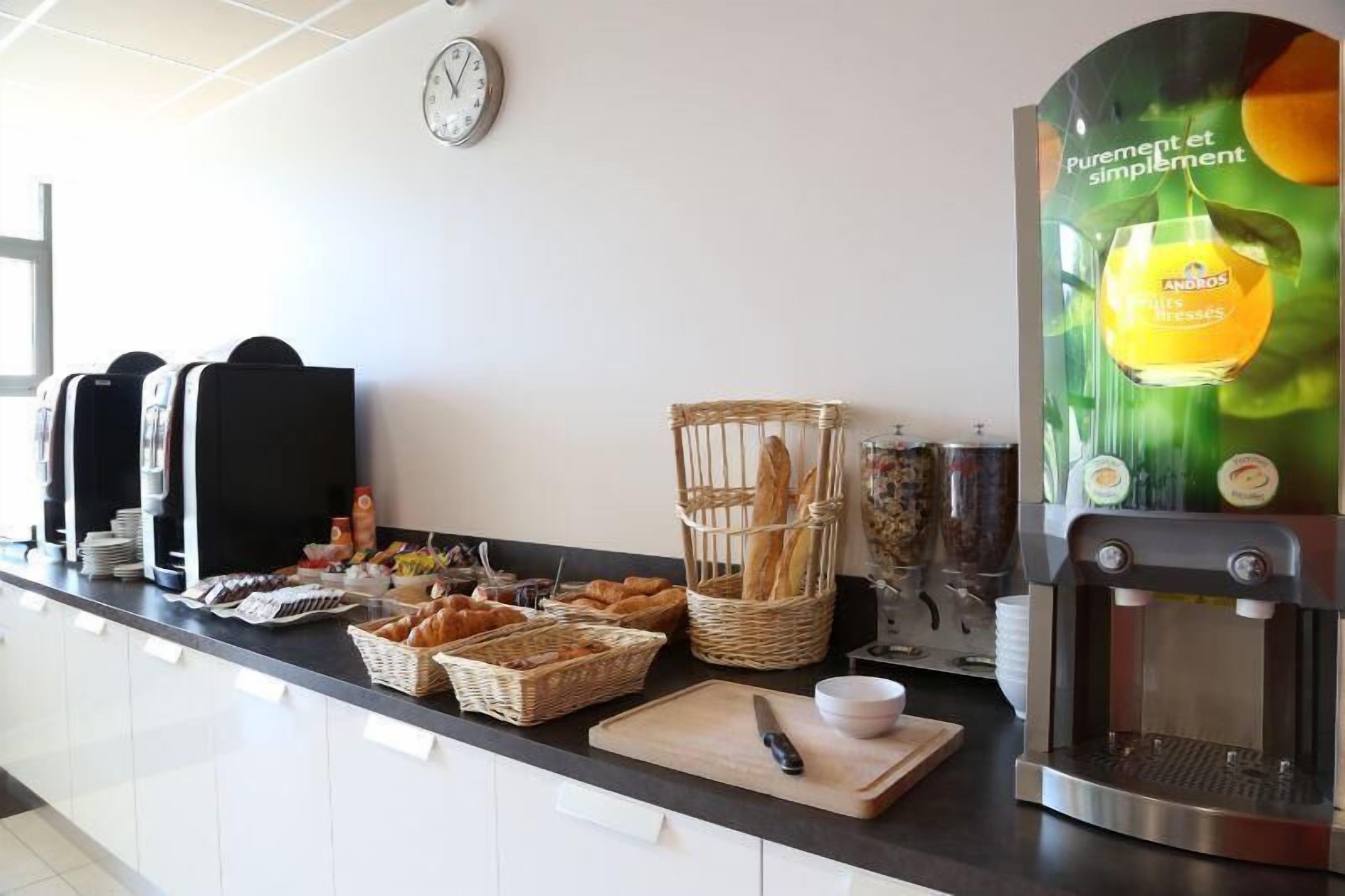 A breakfast buffet area with various food items, a coffee machine, and a clock on the wall.