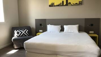 Habitación de hotel con cama, una silla, mesita de noche y una obra de arte en la pared.
