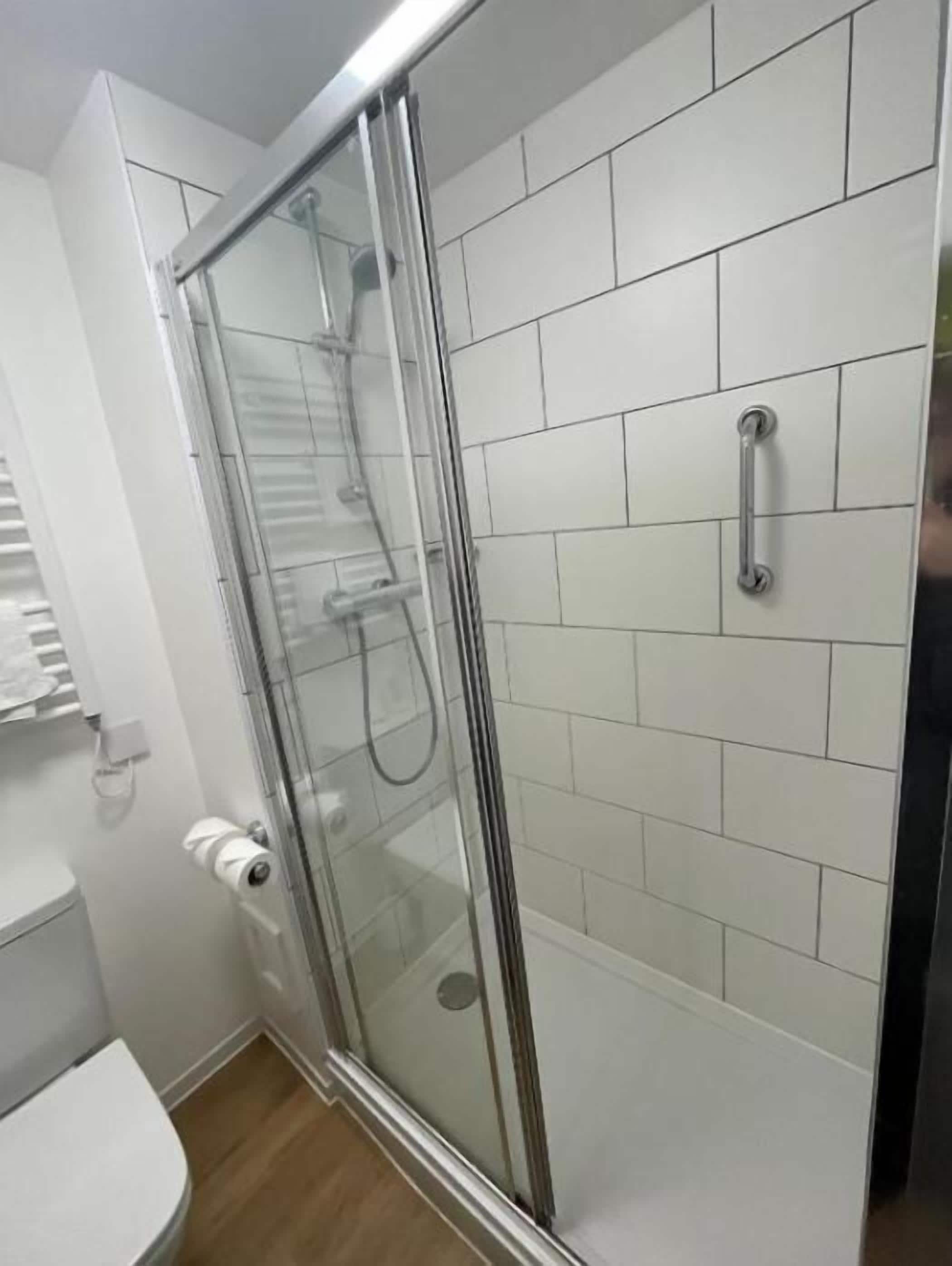 A shower enclosure with a glass door, a toilet, and white tiled walls.