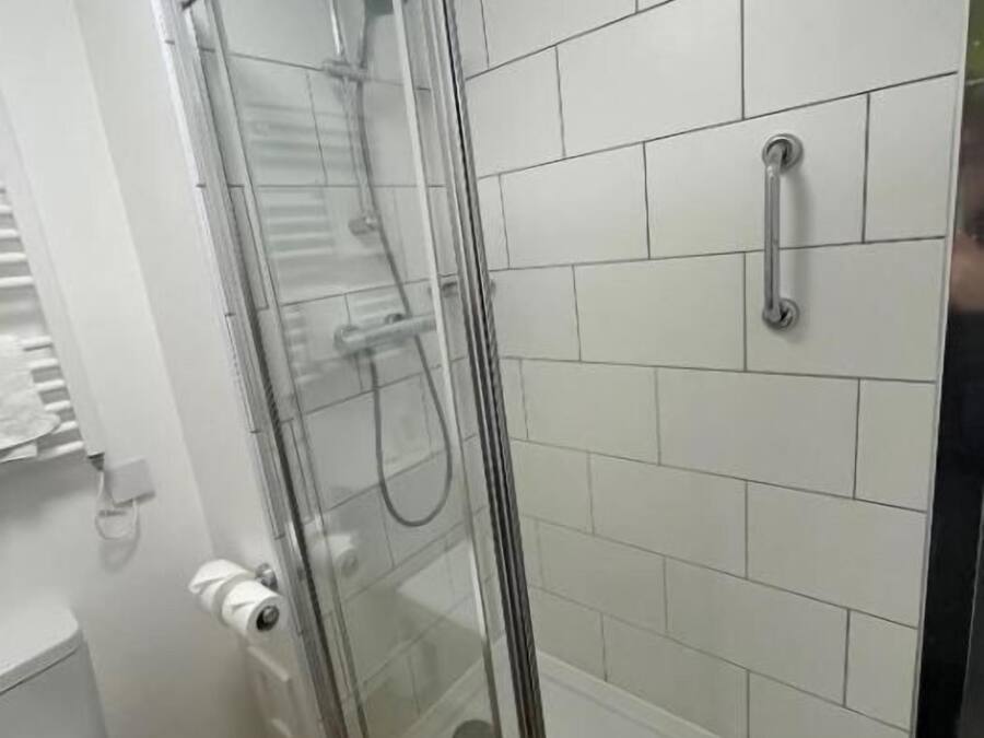 A shower enclosure with a glass door, a toilet, and white tiled walls.