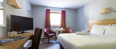 Habitación de hotel con cama, escritorio con televisor, silla, mesita y ventana con cortinas.