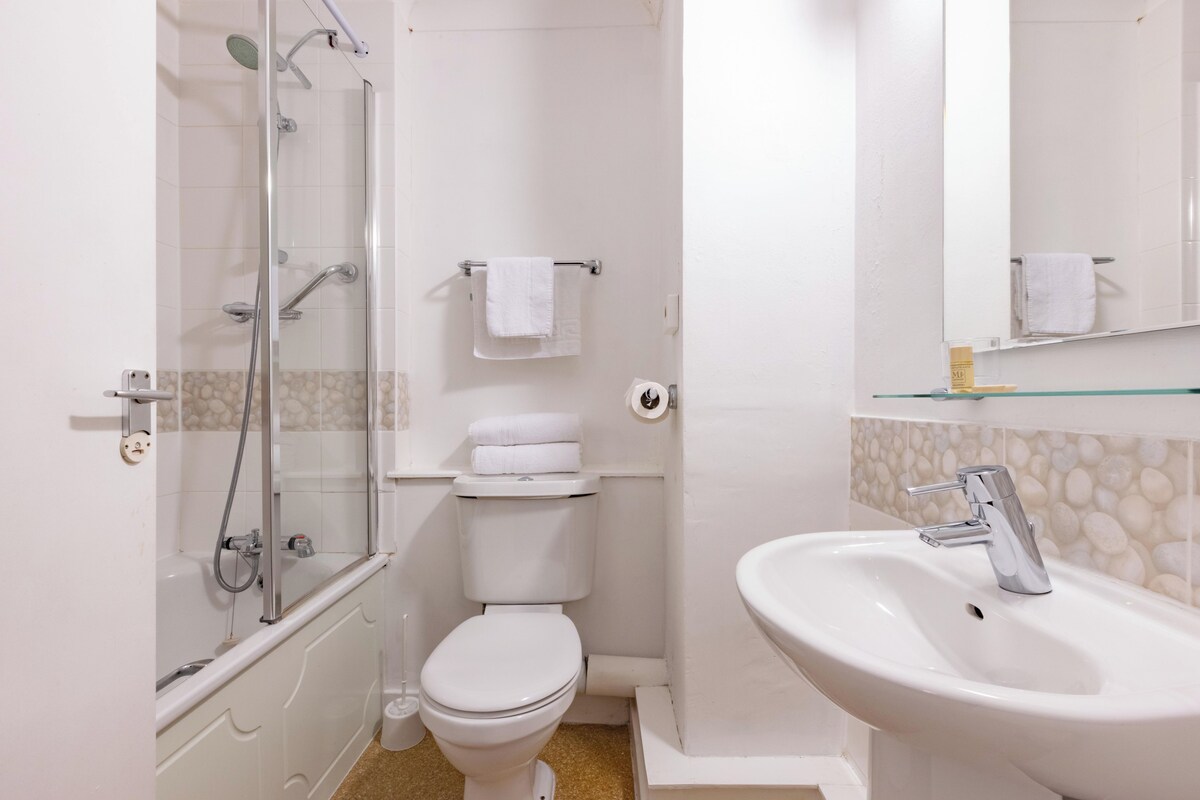 A modern bathroom with a glass-enclosed shower, a white toilet, and a sink with a mirror above it.