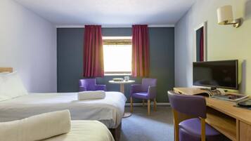 Habitación de hotel con dos camas, un escritorio con televisor, una silla y una ventana con cortinas.