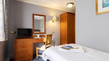 A hotel room with a bed, a desk with a computer, a chair, a wardrobe, and a mirror.
