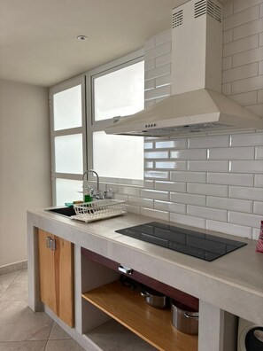 Una cocina moderna con estufa integrada, una ventana sobre el lavabo y salpicadero de azulejos blancos.