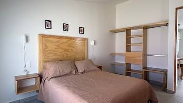 A bedroom with a wooden headboard, a bed with a textured blanket, a nightstand with a lamp, and a built-in shelving unit.