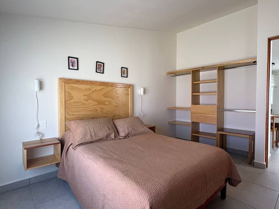 A bedroom with a wooden headboard, a bed with a textured blanket, a nightstand with a lamp, and a built-in shelving unit.