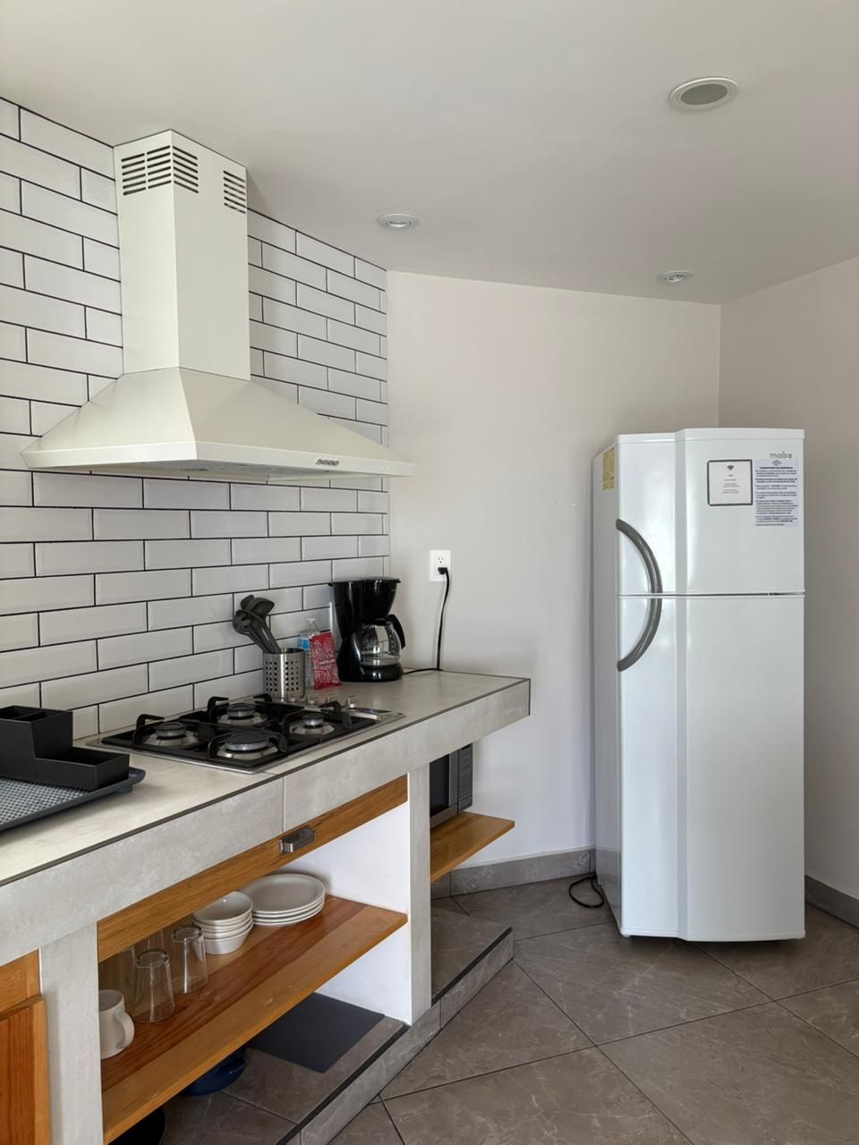 A kitchen with a gas stove, white tiles, a white range hood, a white refrigerator, and wooden shelves.