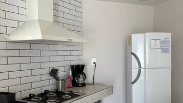 A kitchen with a gas stove, white tiles, a white range hood, a white refrigerator, and wooden shelves.