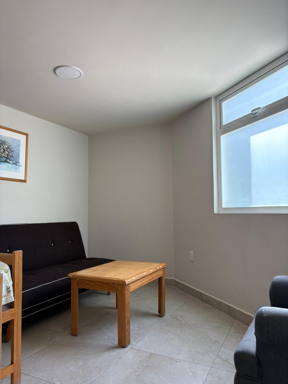A room with a black sofa, a wooden table, and a window.