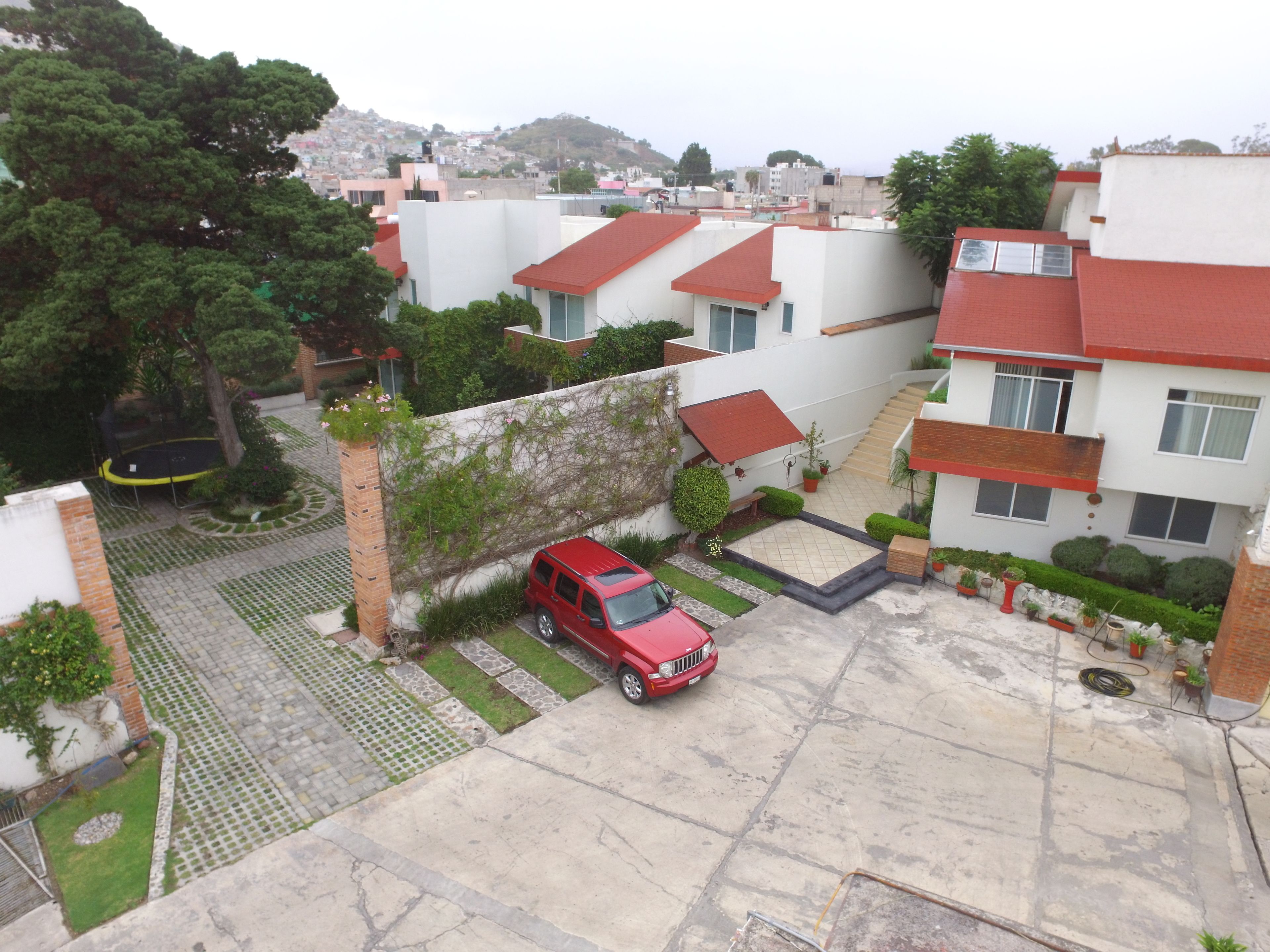 Un quartier résidentiel où une voiture rouge est garée dans une allée, entouré de maisons modernes aux toits rouges et aux murs blancs.