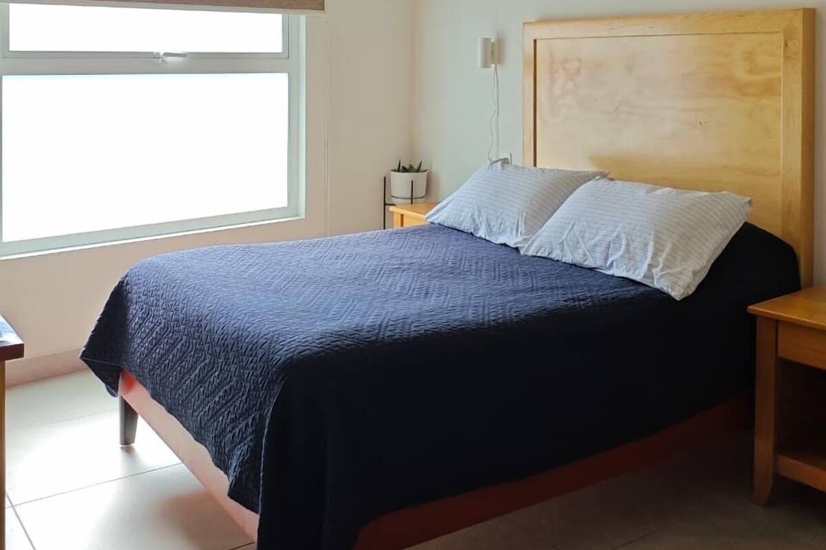 A bedroom with a bed, a nightstand, a window, and a ceiling light.