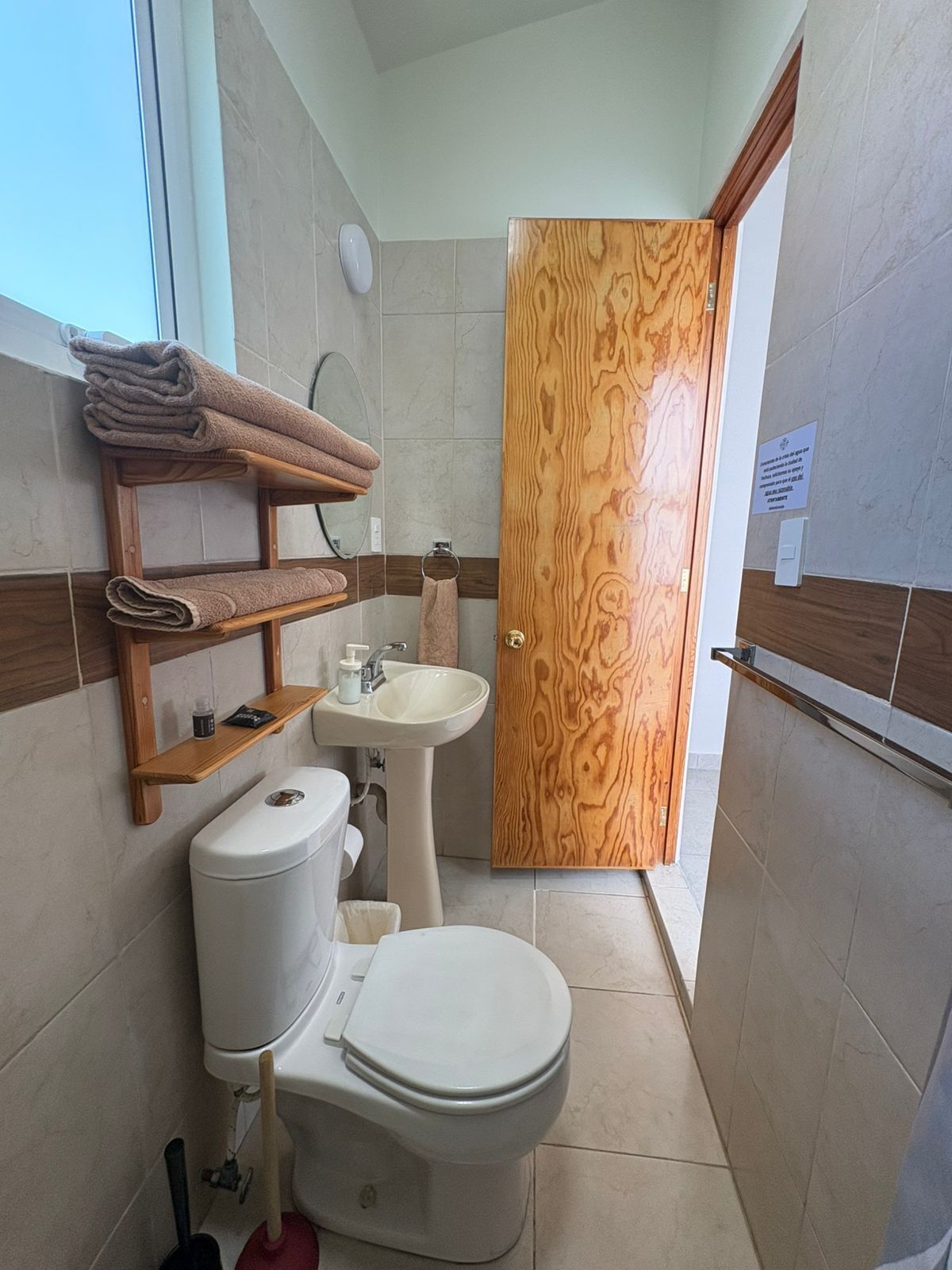 Un baño con inodoro, lavamanos, estantes de madera y una puerta de madera.