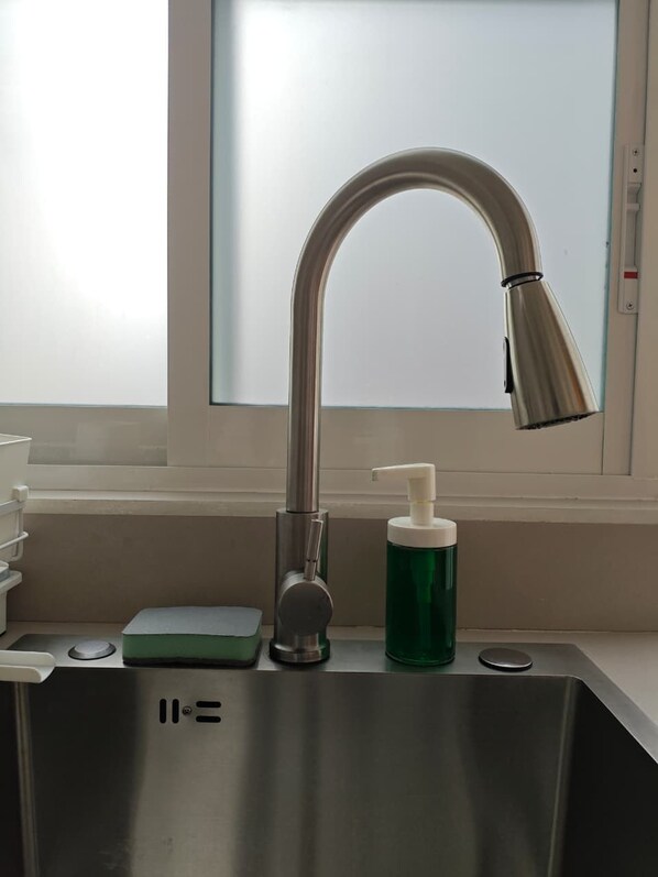 Un lavamanos de acero inoxidable con un grifo moderno, un dispensador de jabón y una botella de jabón verde.