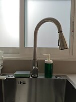 A stainless steel sink with a modern faucet, a soap dispenser, and a green soap bottle.