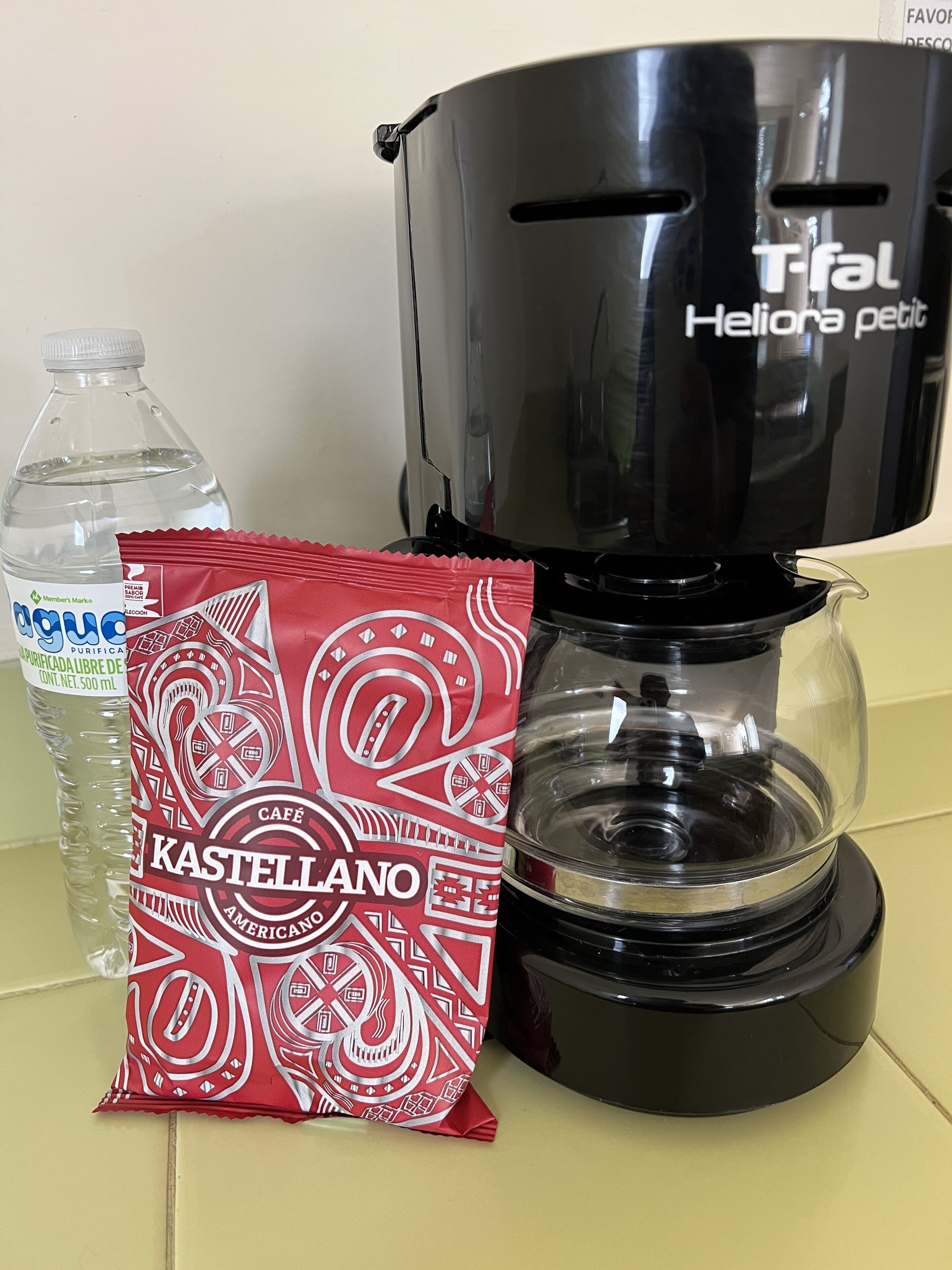 A coffee maker, a water bottle, and a packet of coffee creamer.
