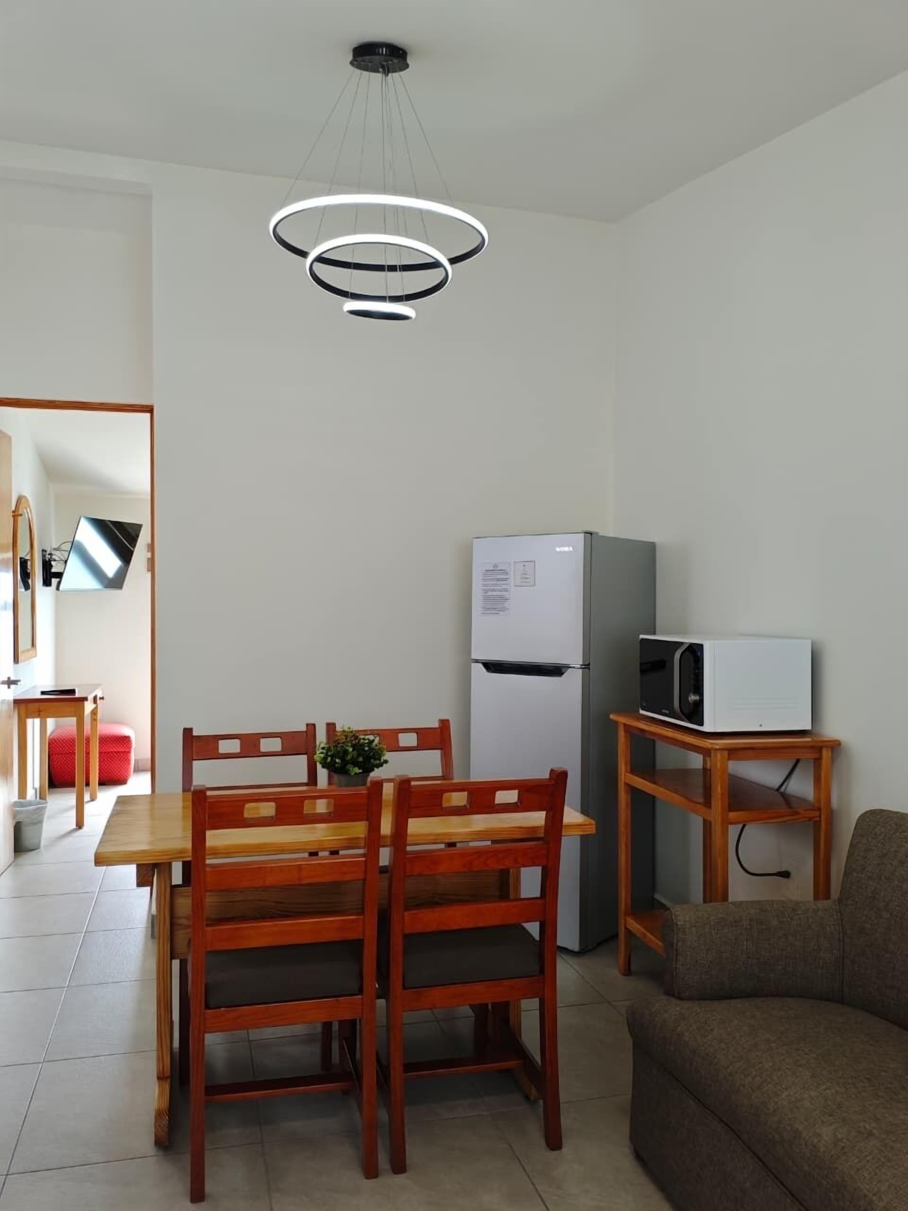 A compact kitchen with a dining table, chairs, a refrigerator, a microwave, and a sofa.