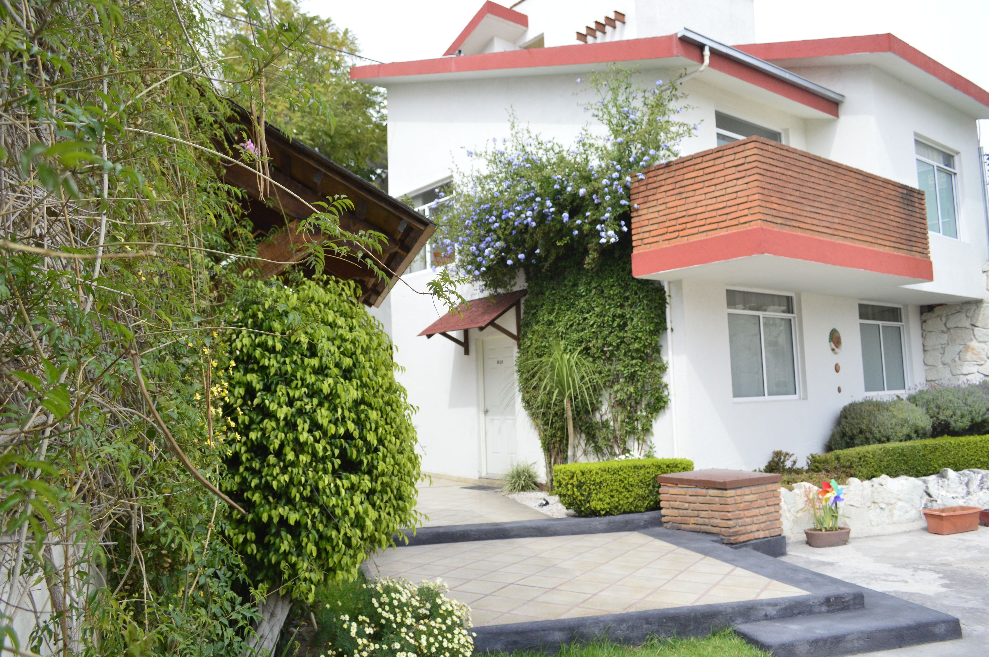 Una casa moderna de dos pisos con fachada blanca, techo rojo y un pequeño porche delantero.