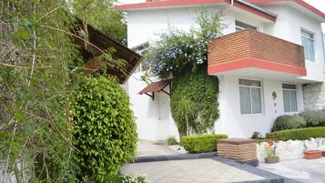Una casa moderna de dos pisos con fachada blanca, techo rojo y un pequeño porche delantero.