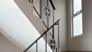 A staircase with a black metal railing and decorative elements, leading to a landing with a potted plant. - Privada 400 Casas & Suites (Pachuca)