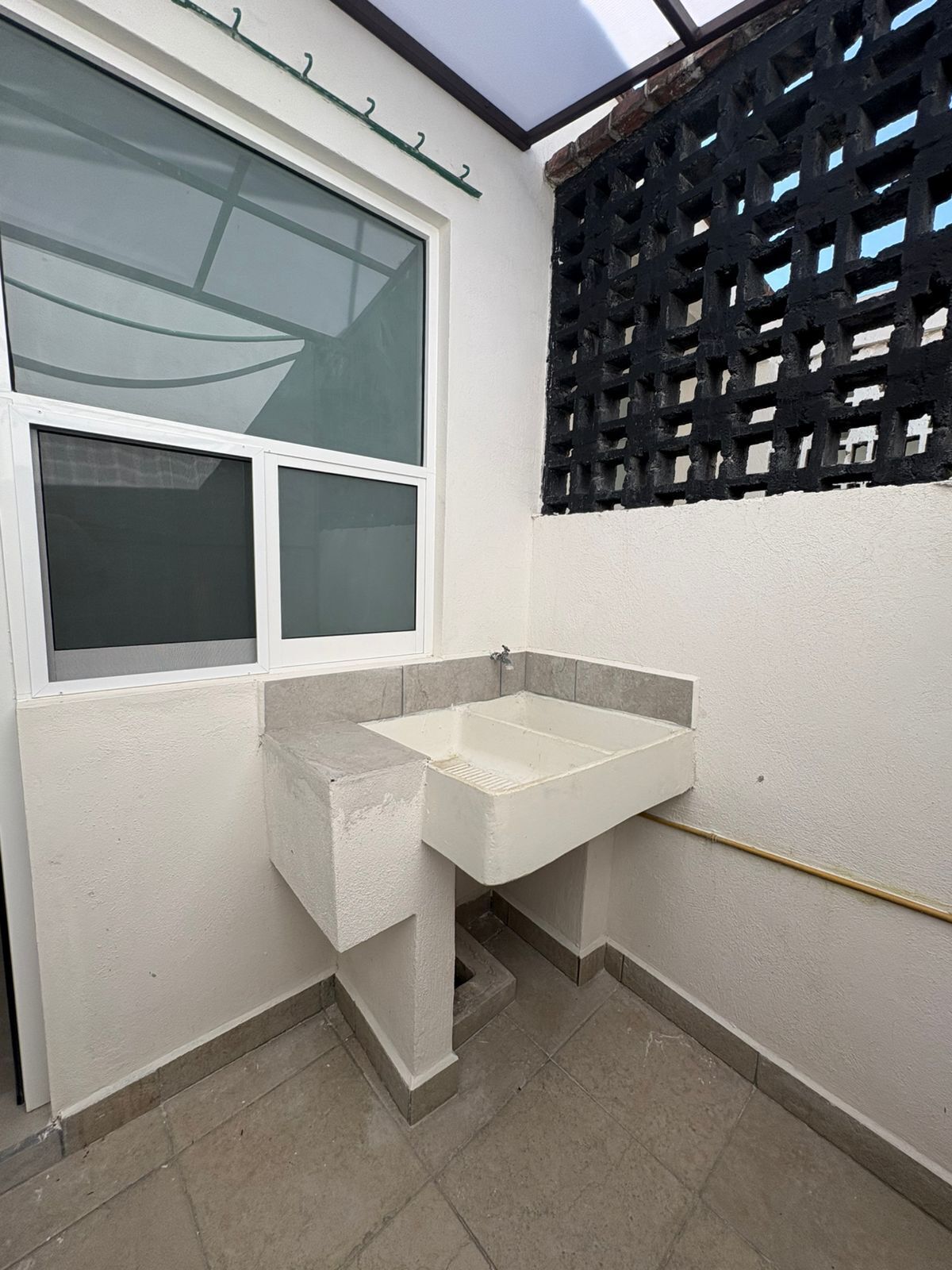 A small bathroom with a white sink, a window, and a black lattice partition.