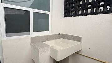A small bathroom with a white sink, a window, and a black lattice partition.