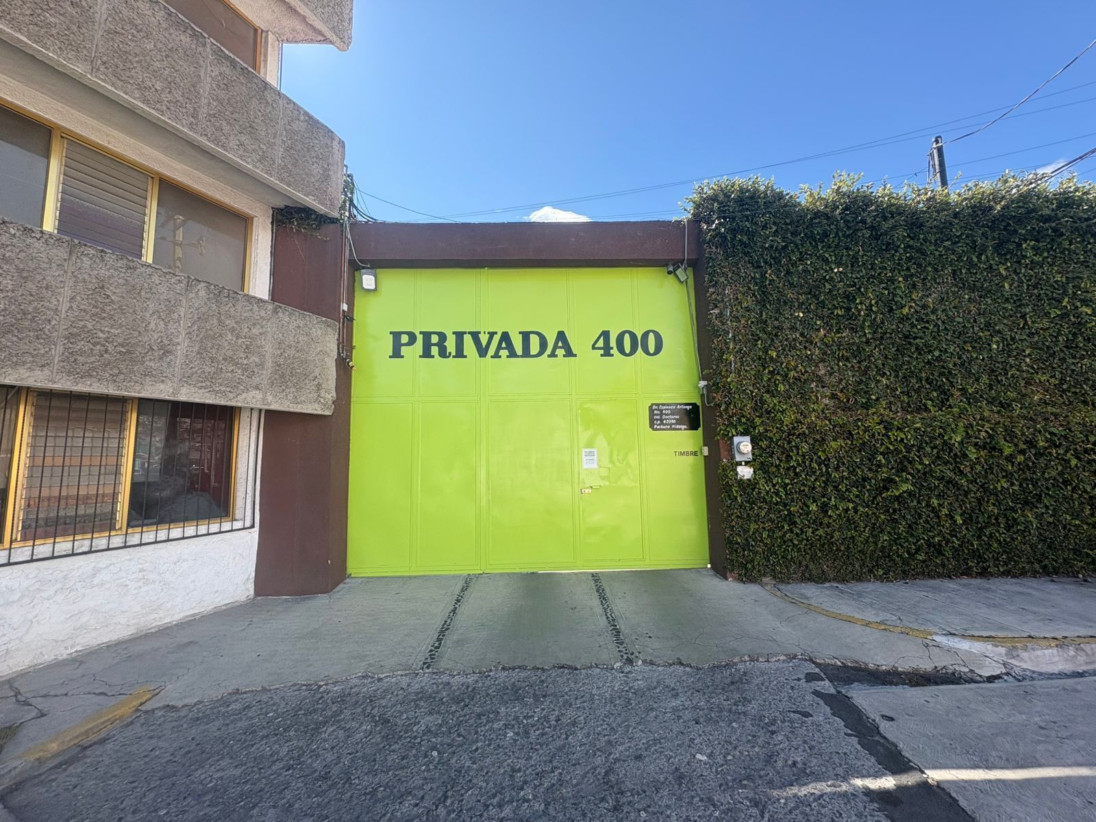 Entrada de un edificio con una puerta verde que indica 'PRIVADA 400' y un pequeño letrero con información de contacto.