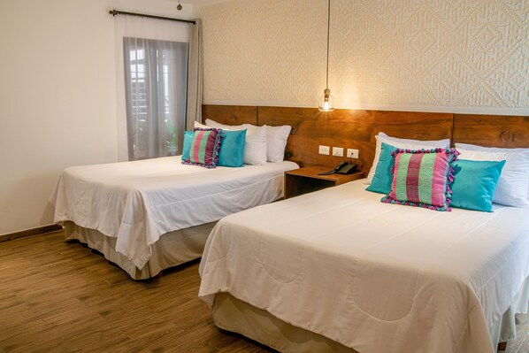 Two single beds with white linens and colorful pillows, a wooden headboard, a bedside table with a phone, and a window with sheer curtains. - Hotel Camelias Inn by AHS (Antigua Guatemala)