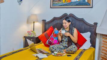 Una cama con una colcha amarilla, una computadora portátil, un libro y un plato de comida.