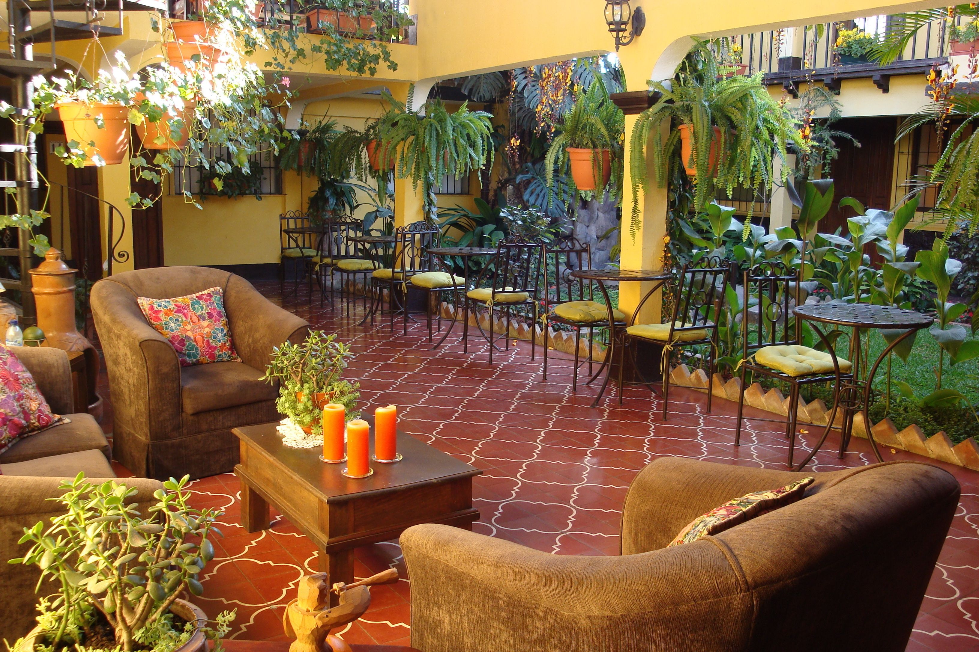 A cozy patio area with multiple seating arrangements, including sofas and chairs, surrounded by lush greenery and potted plants.