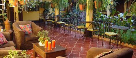 A cozy patio area with multiple seating arrangements, including sofas and chairs, surrounded by lush greenery and potted plants.