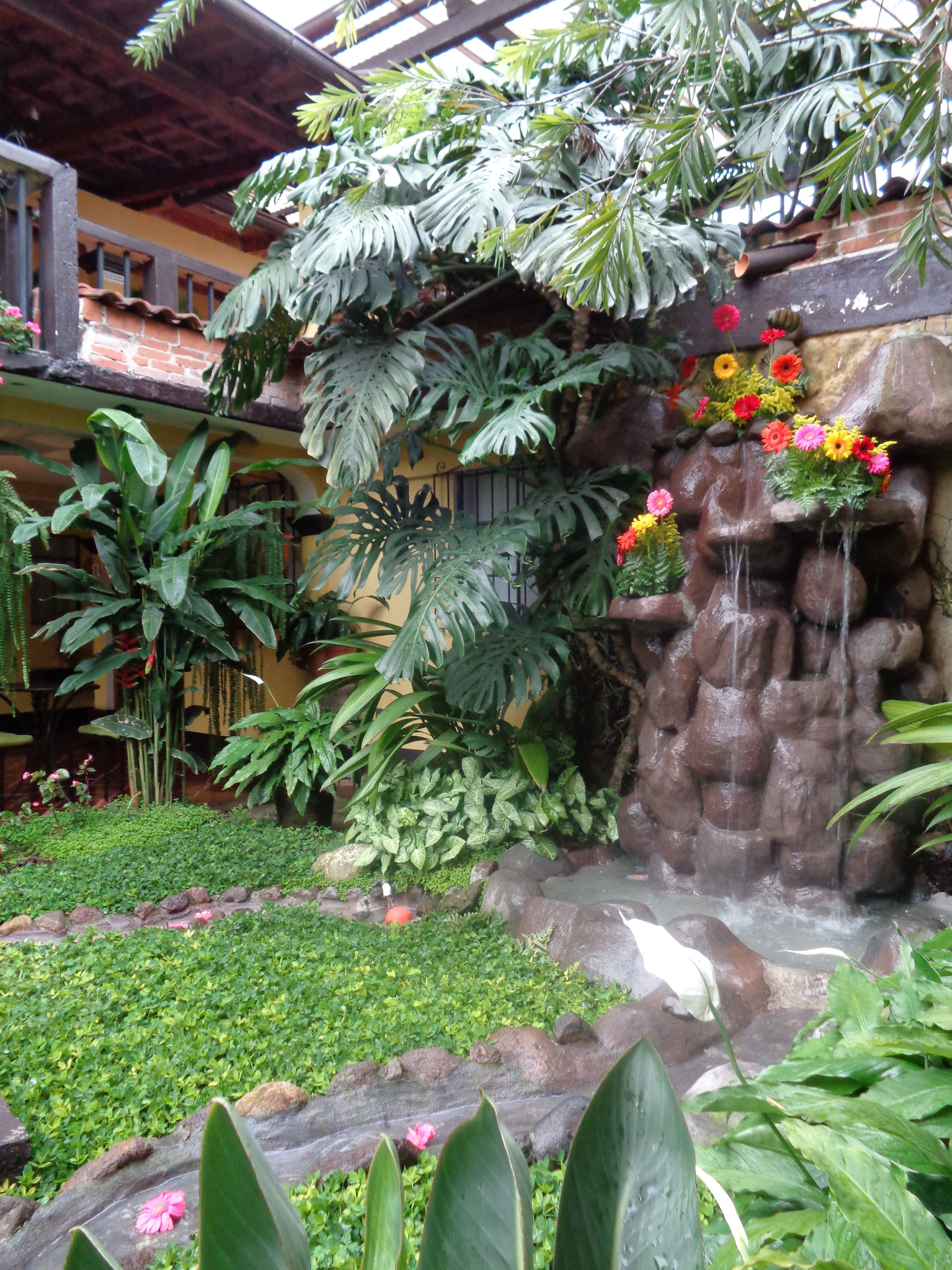 Un jardín con cascada de rocas, abundante vegetación y plantas con flores.