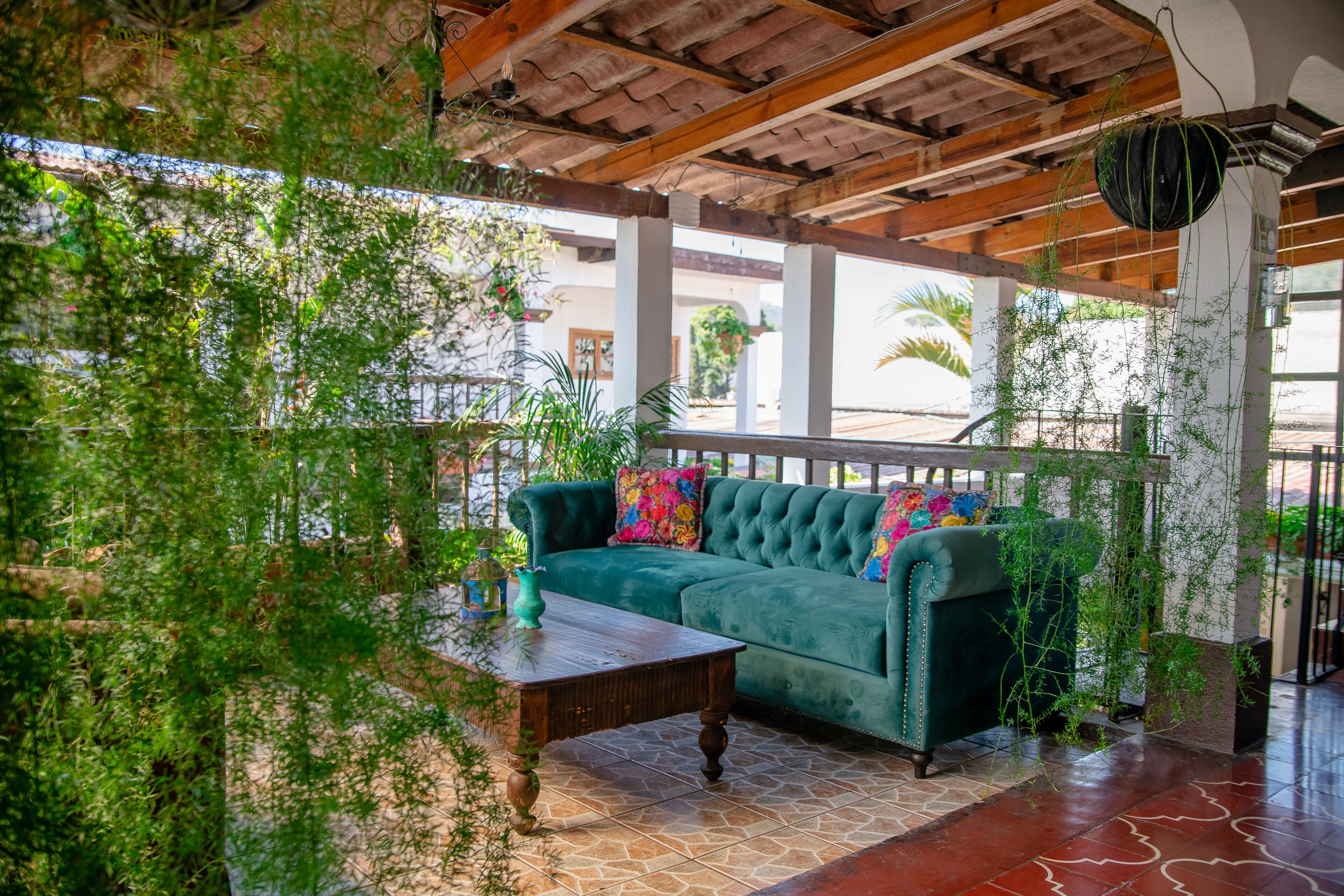 Un espacio patio acogedor con un sofá verde, una mesa de centro de madera y plantas colgantes.